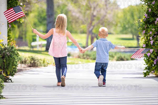 Young sister and brother holding hands and waving american flags at the park