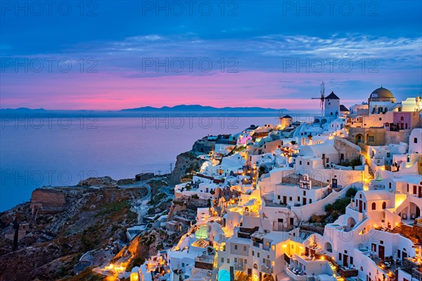 Famous greek iconic selfie spot tourist destination Oia village with traditional white houses and windmills in Santorini island in the evening blue hour