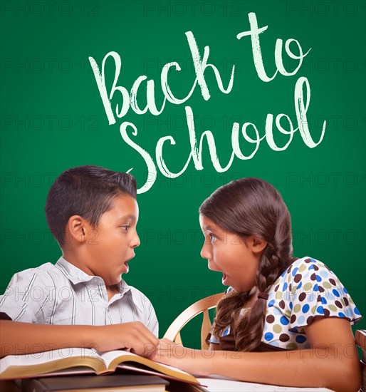 Back to school written on chalk board behind hispanic boy and girl having fun studying together