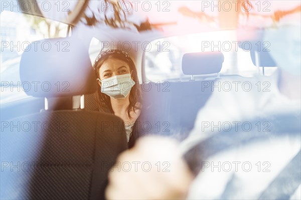 A woman wearing a protective mask sitting on the back seat of a taxi car