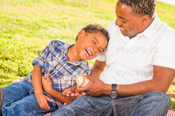 African american father and mixed-race son playing with baseball in the park