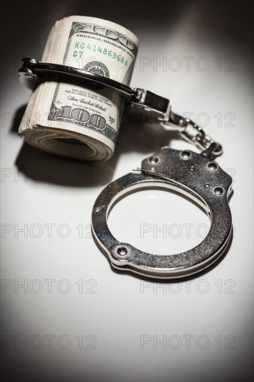 Handcuffs locked on roll of one hundred dollar bills under spotlight