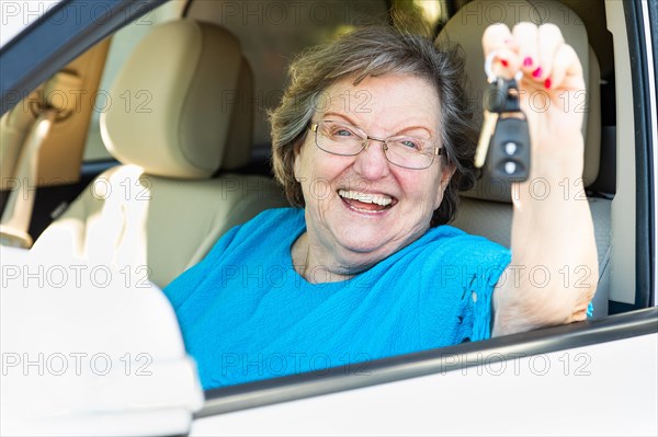 Happy senior woman sitting in new car holding the keys