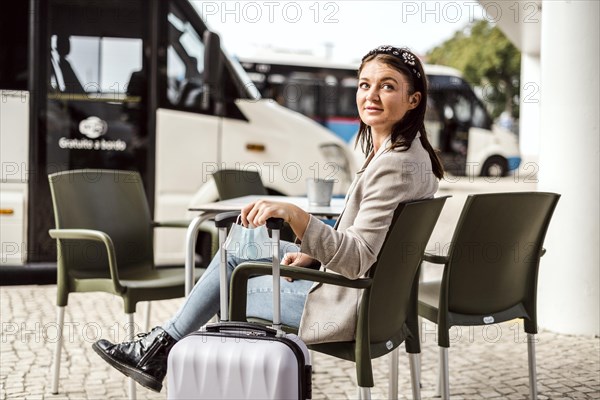 A young traveler with the luggage and protective mask sitting in the cafe and waiting for her bus to come