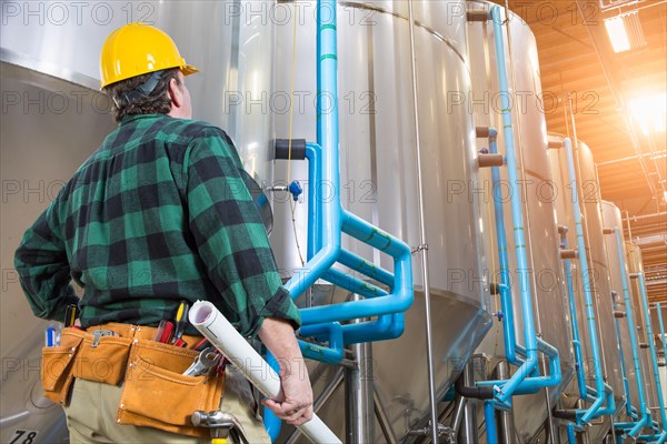 Man wearing hard hat looking up at large industrial tanks