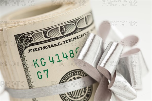 Roll of one hundred dollar bills with silver bow on white