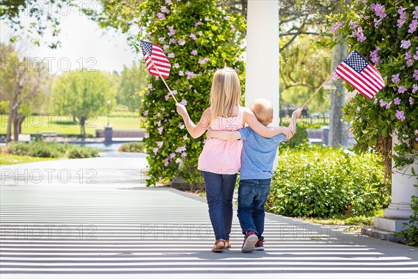 Young sister and brother waving american flags at the park