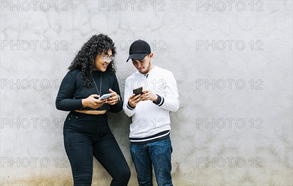 Two teenage friends checking their cell phones and smiling