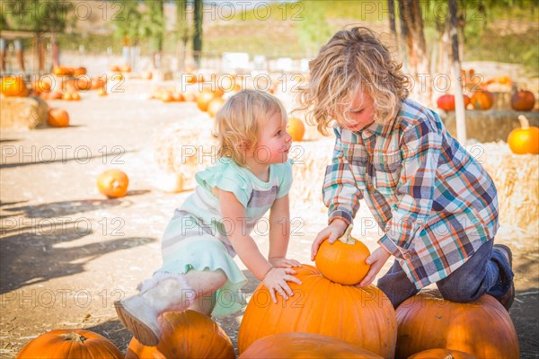 Sweet little boy plays with his baby sister in a rustic ranch setting at the pumpkin patch