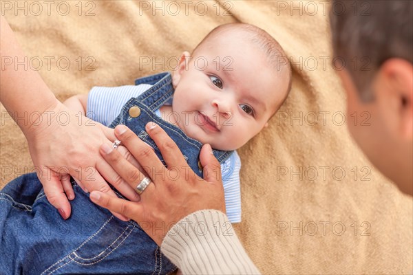 Young mixed-race couple laying with their infant on A blanket