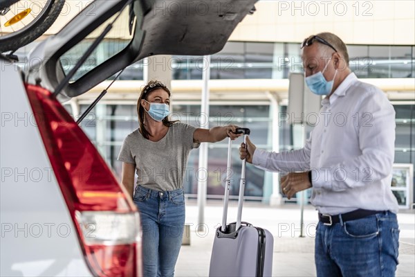 A taxi or Uber driver helping a passenger in a protective mask with her luggage at the airport