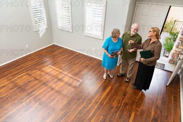 Female real estate agent handing new house keys to senior adult couple in new home