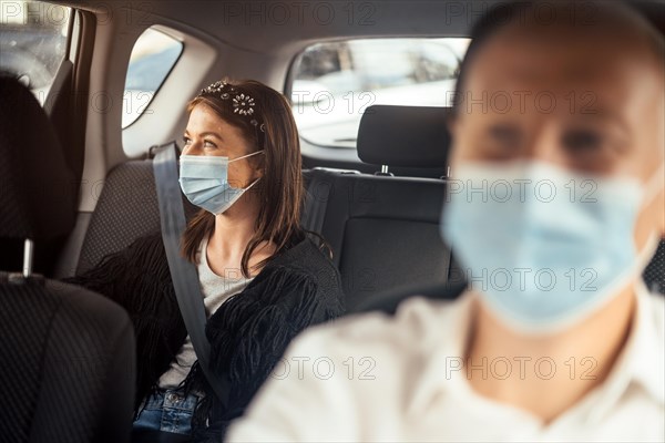 A woman wearing a protective mask sitting on the back seat of a taxi car