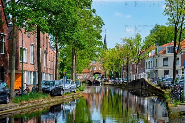 Cars and bicycles parked along the canal in street of Delft with reflection