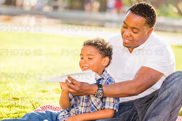 Happy african american father and mixed-race son playing with paper airplanes in the park
