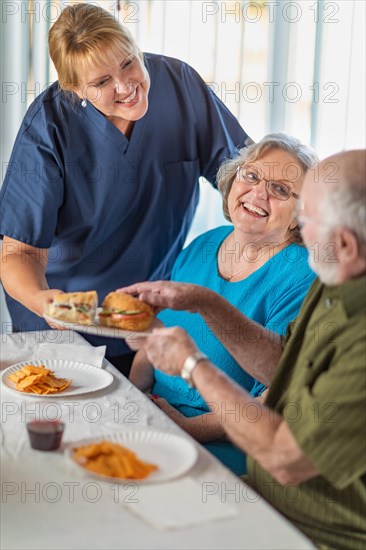 Female doctor or nurse serving senior adult couple sandwiches at table