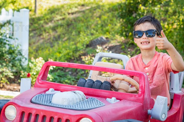 Young mixed-race chinese and caucasian boy wearing sunglasses playing in toy car