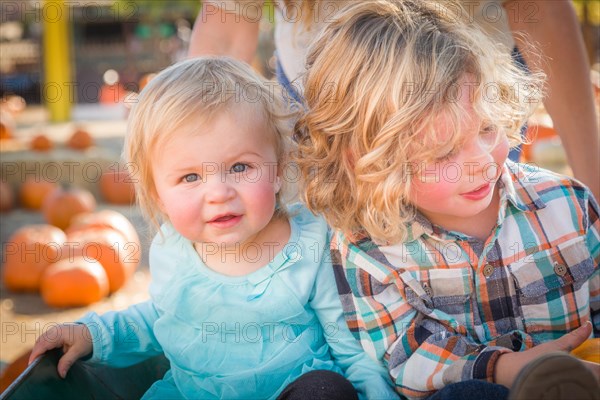 Sweet little boy plays with his baby sister in a rustic ranch setting at the pumpkin patch