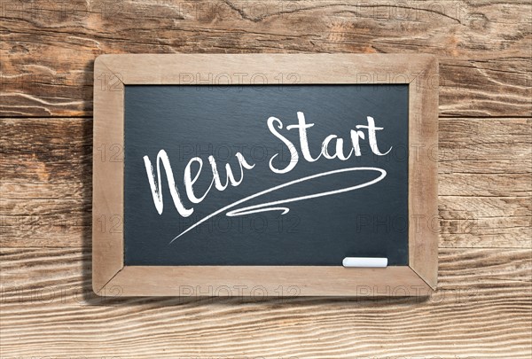 New start written on slate chalk board against aged wood background