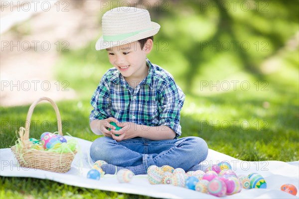 mixed-race chinese and caucasian boy outside wearing rabbit ears playing with easter eggs