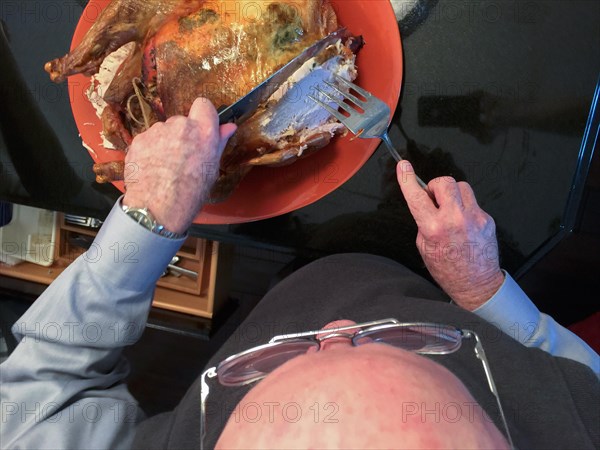 Senior adult man cutting the delicious holiday Turkey in the kitchen