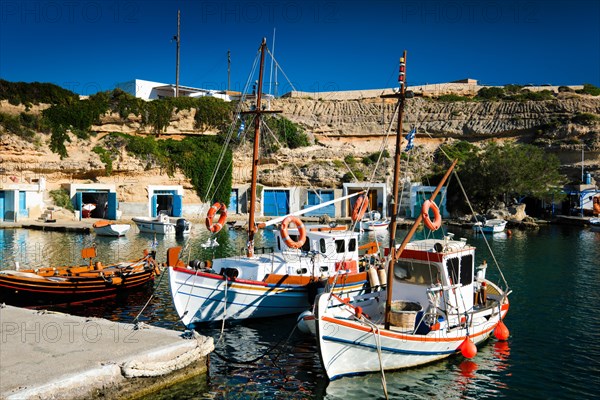 Fishing boats moored in crystal clear turquoise sea water in harbour in Greek fishing village of Mandrakia