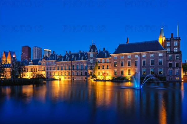 View of the Binnenhof House of Parliament and the Hofvijver lake with downtown skyscrapers in background illuminated in the evening