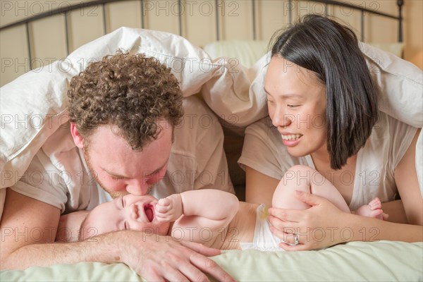 mixed-race chinese and caucasian baby boy laying in bed with his father and mother