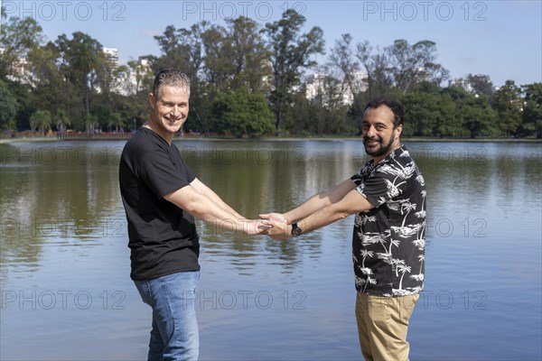 Homosexual mature white male couple holding hands smiling at a lake