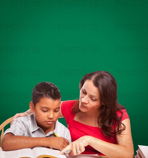 Blank chalk board behind hispanic young boy and famale adult studying