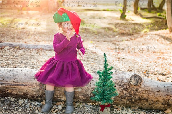 Cute mixed-race young baby girl having fun with christmas hat and tree outdoors