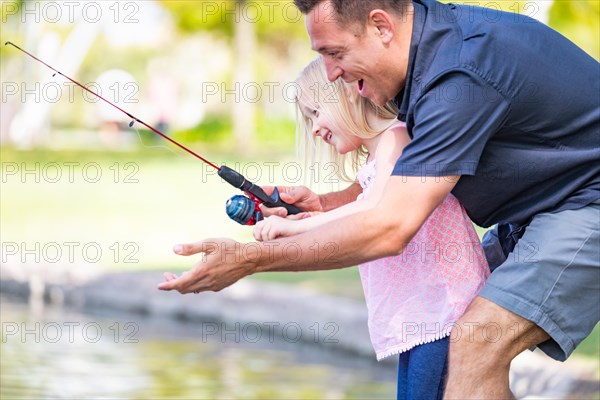 Young caucasian father and daughter having fun fishing at the lake