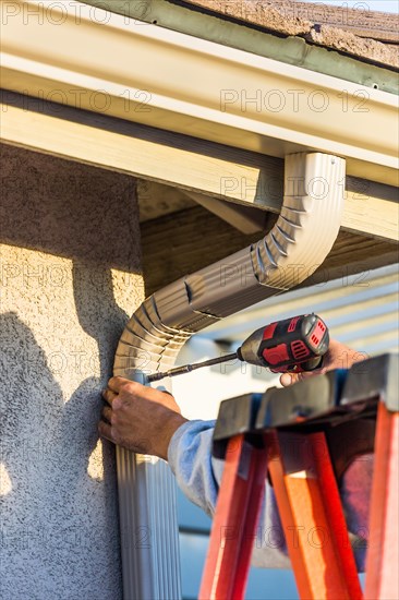 Worker attaching aluminum rain gutter and down spout to fascia of house