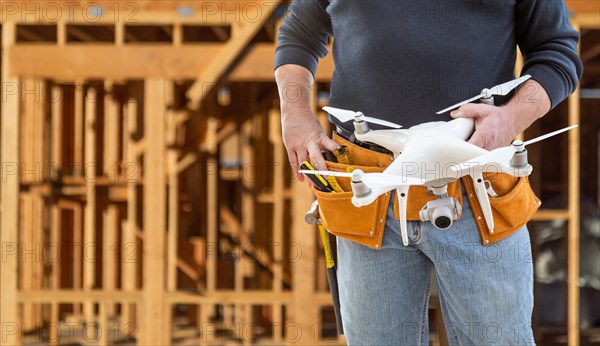 Construction worker and drone pilot with toolbelt holding drone at construction site