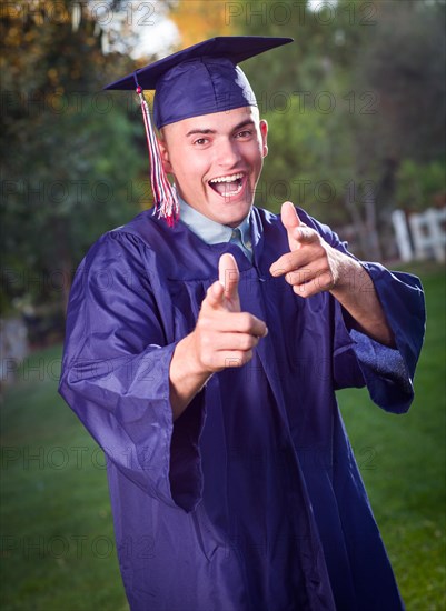 Happy handsome male graduate in cap and gown outside