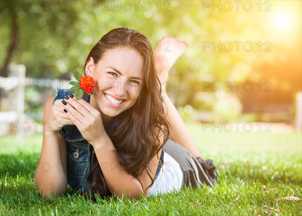 Attractive mixed-race girl daydreaming laying in grass outdoors with flower