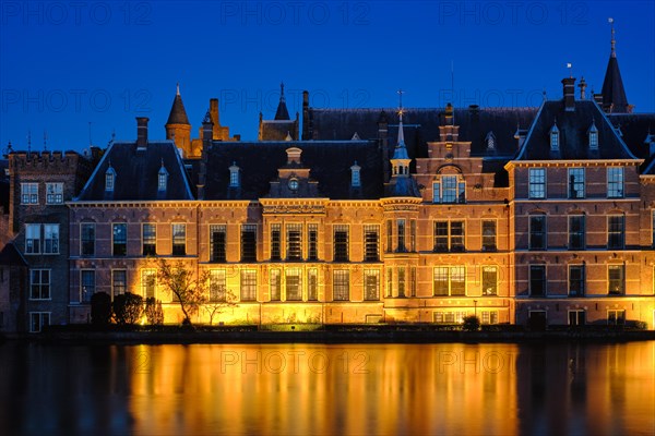 View of the Binnenhof House of Parliament and the Hofvijver lake with downtown skyscrapers in background illuminated in the evening. The Hague