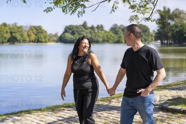 Multi-ethnic couple formed by an Andean woman and a Caucasian man walking by a lake. Happy expressions and faces of lovers