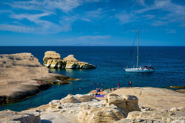 Yacht boat at famous Sarakiniko beach white rocks tourist attraction with tourists on beach in Aegean sea on sunset