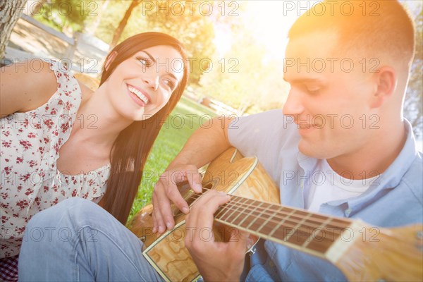 Happy mixed-race couple at the park playing guitar and singing songs