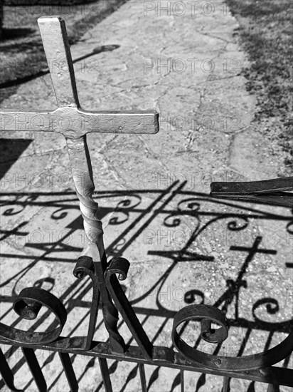 Wrought iron gate with metal cross casting shadows on a path