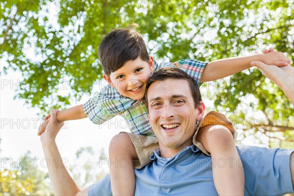 mixed-race father and son playing piggyback together in the park