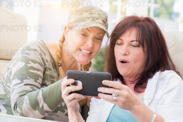 Two female friends laugh while using A smart phone on the patio