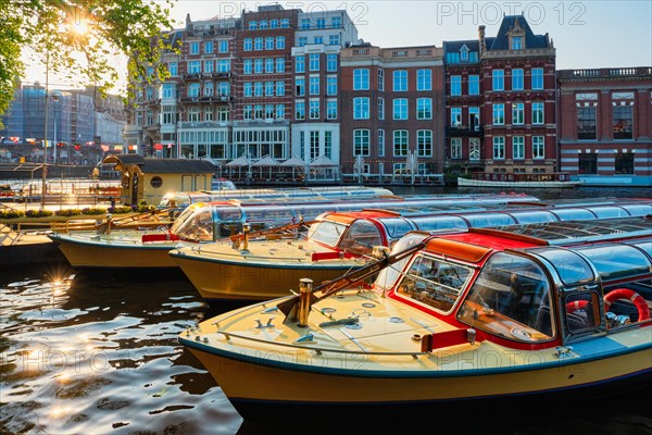 Tourist boats moored in Amsterdam canal pier on sunset. Amsterdam