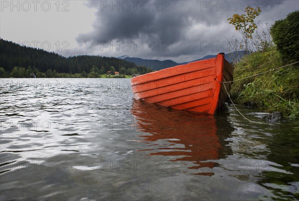 Leeres rote Ruderboot am Seeufer bei Regenwetter