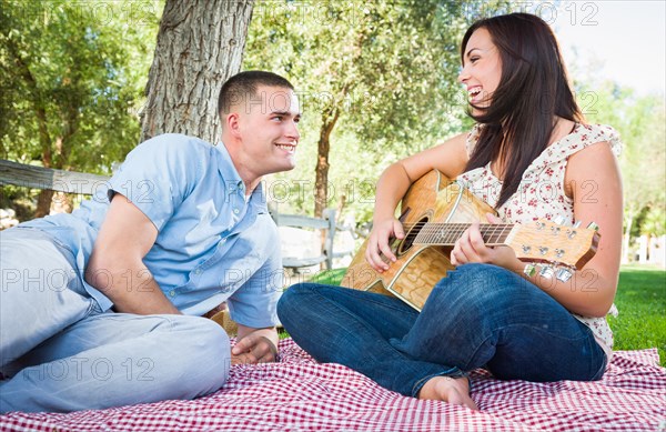 Young adult girl playing guitar with boyfriend in the park