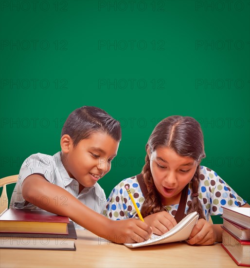 Blank chalk board behind hispanic boy and girl having fun studying together