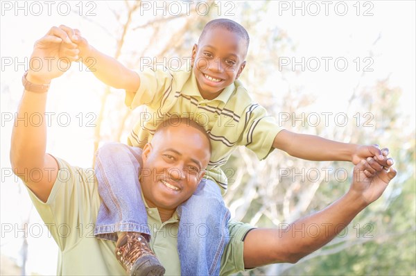 Happy african american father and son riding piggyback outdoors at the park