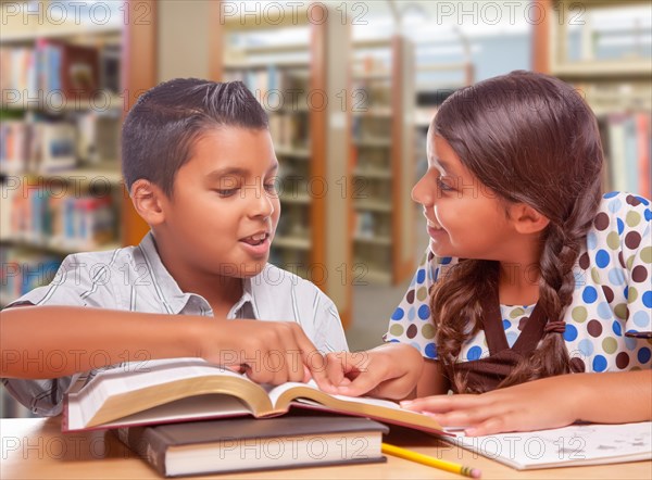 Hispanic boy and girl having fun studying together in the library