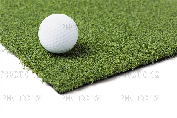 Golf ball resting on section of artificial turf grass on white background